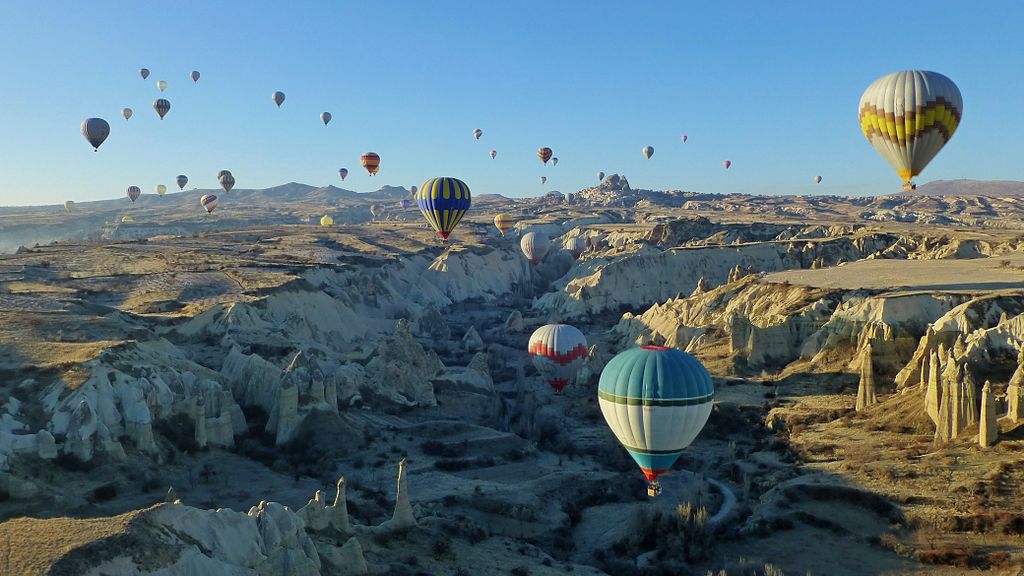 Hot air balloons hover over a scenic valley in Cappadocia, Turkey